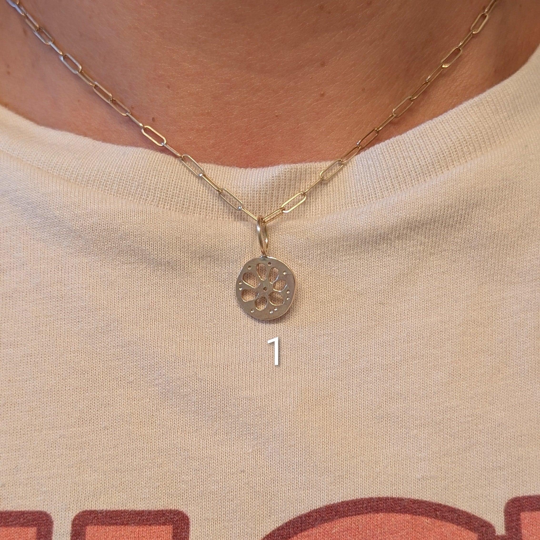 A close-up of a person wearing a delicate gold chain necklace with a circular pendant, paired with a cream-colored graphic t-shirt.