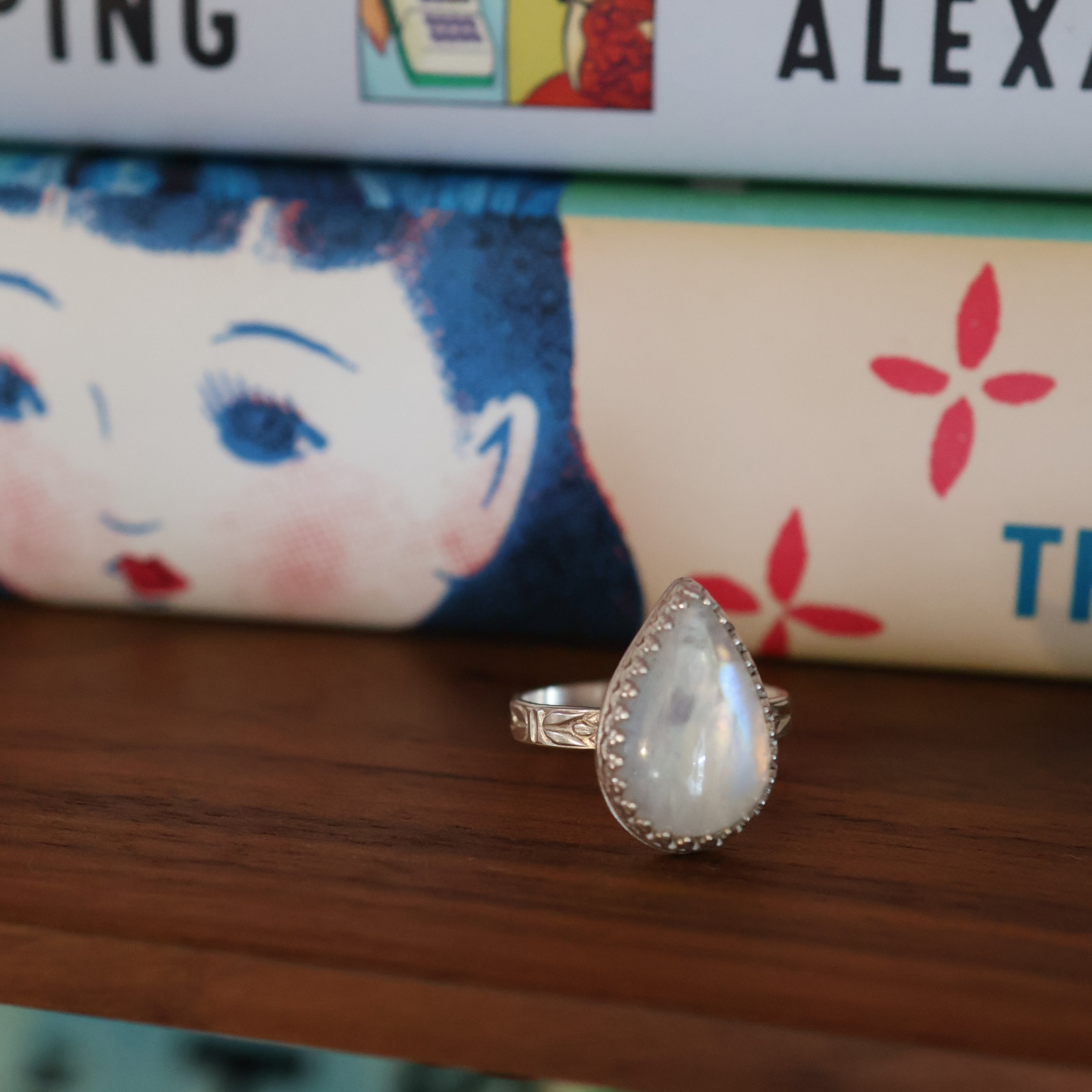 Teardrop-shaped silver and moonstone ring on a wooden surface with books in the background