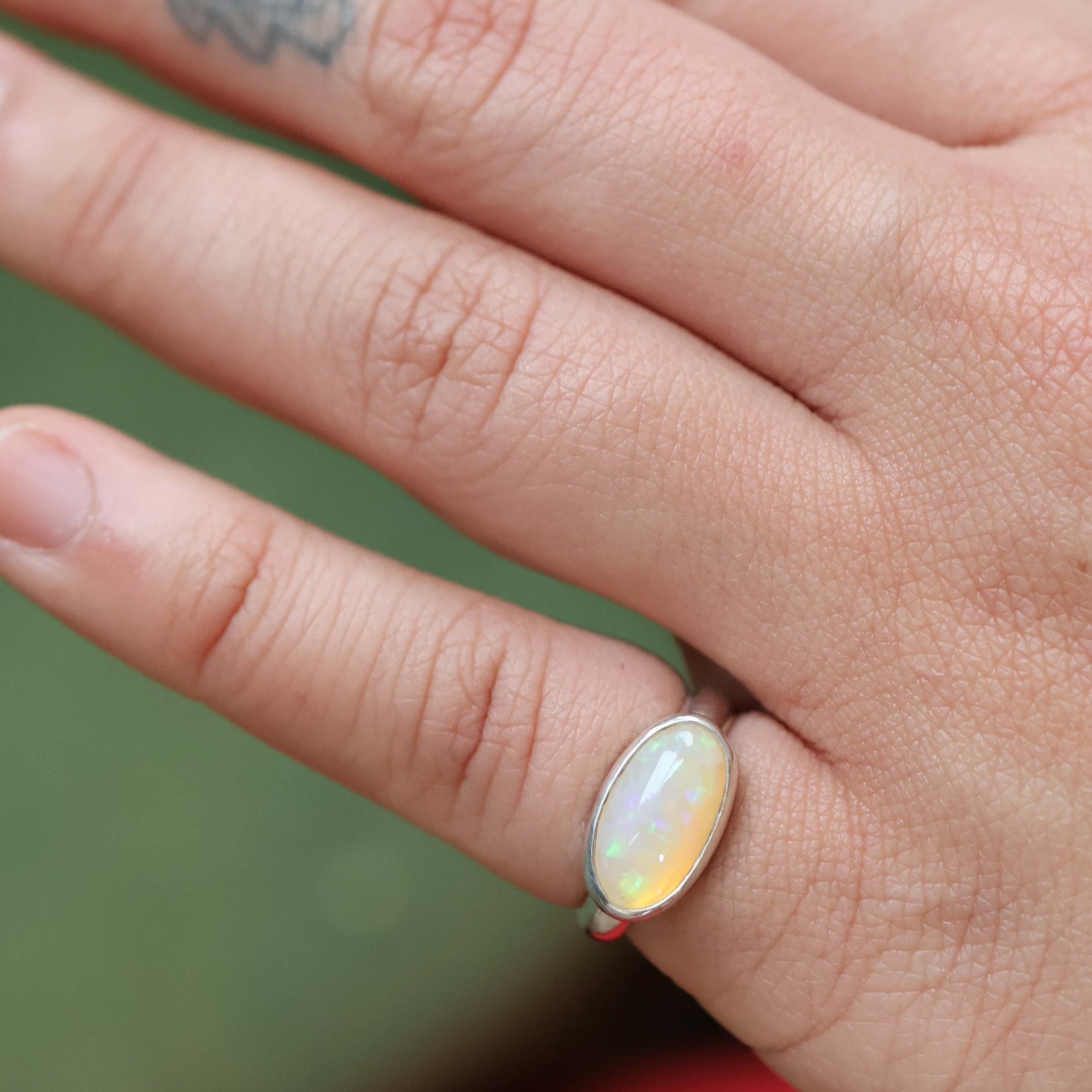 Hand wearing an opal ring with a blurred green background