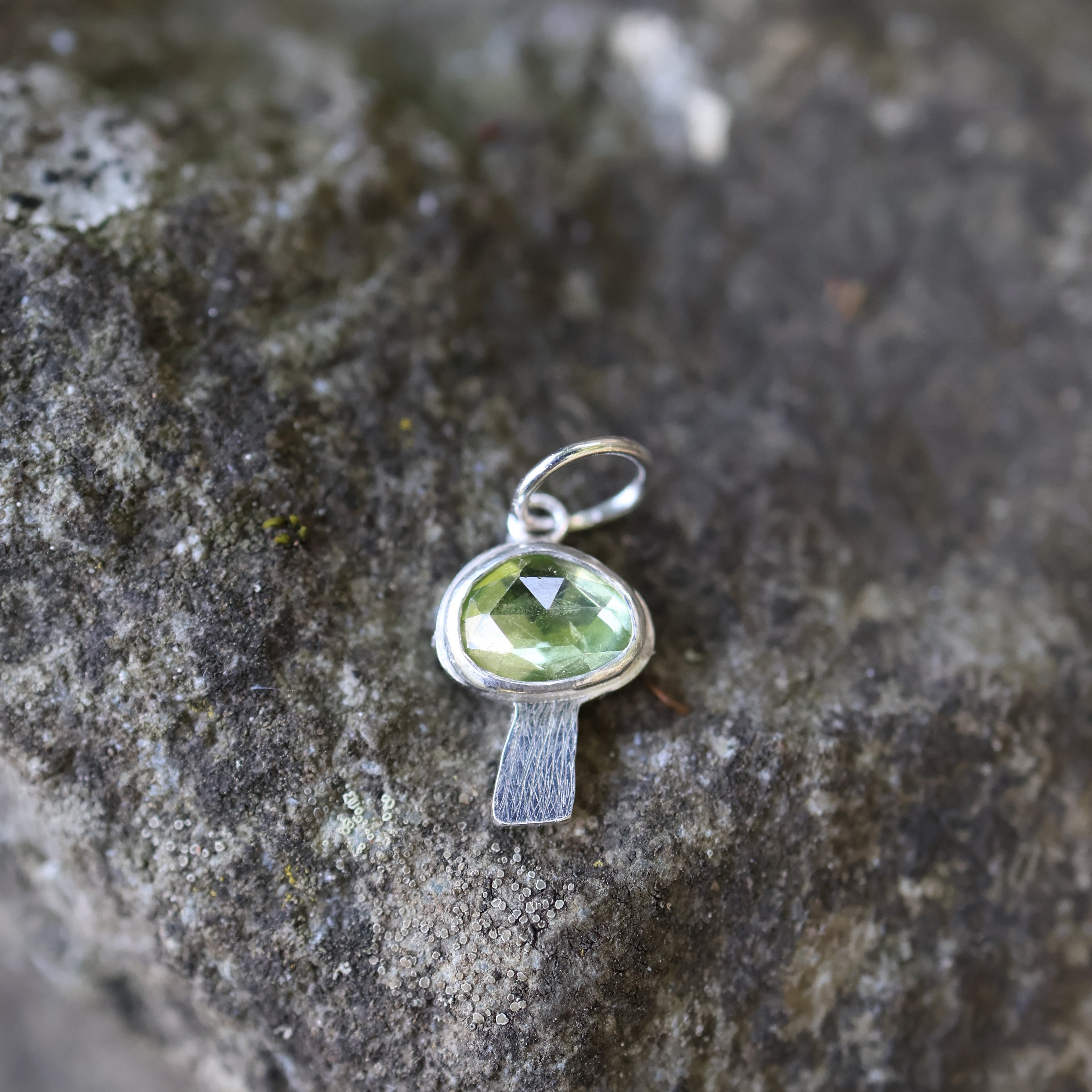 Silver mushroom shaped pendant with a green gemstone on a textured stone surface