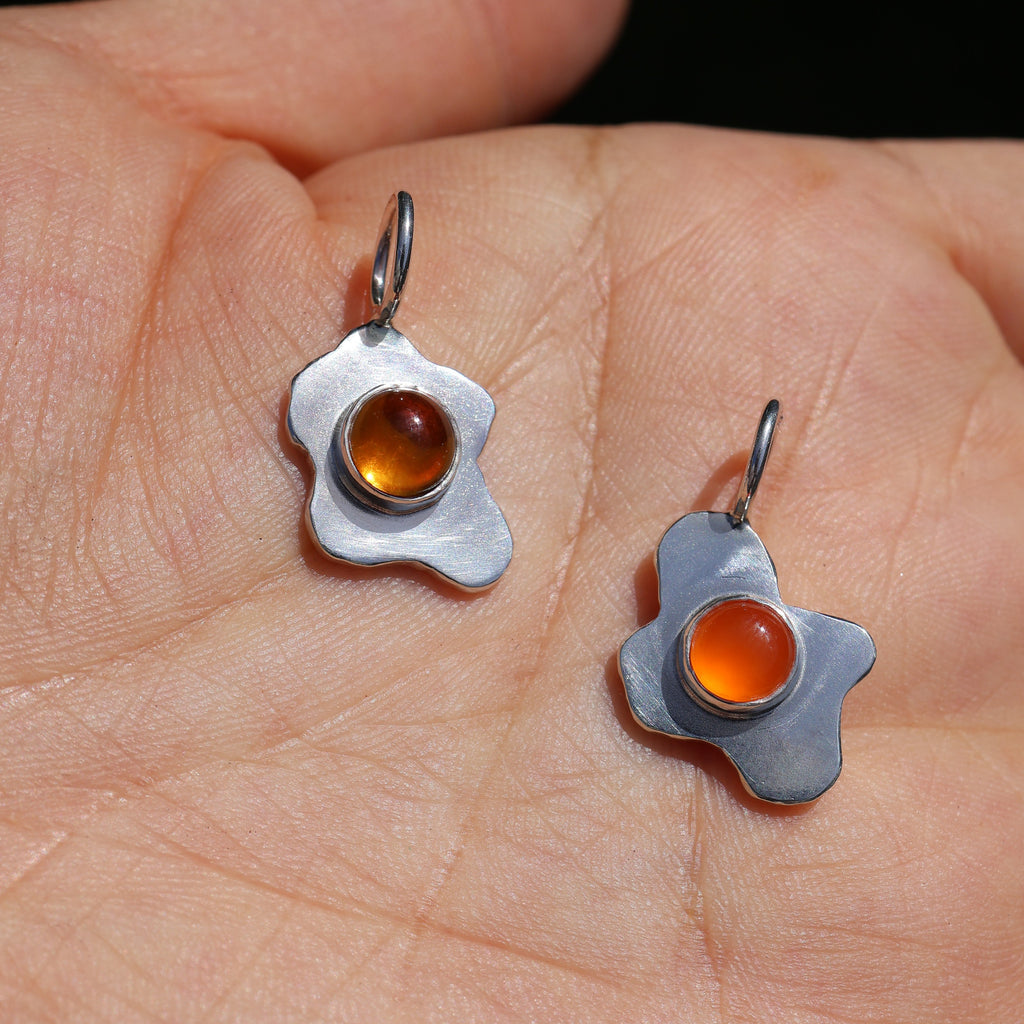 two silver fried egg pendants, one with a citrine stone and one with a carnelian stone