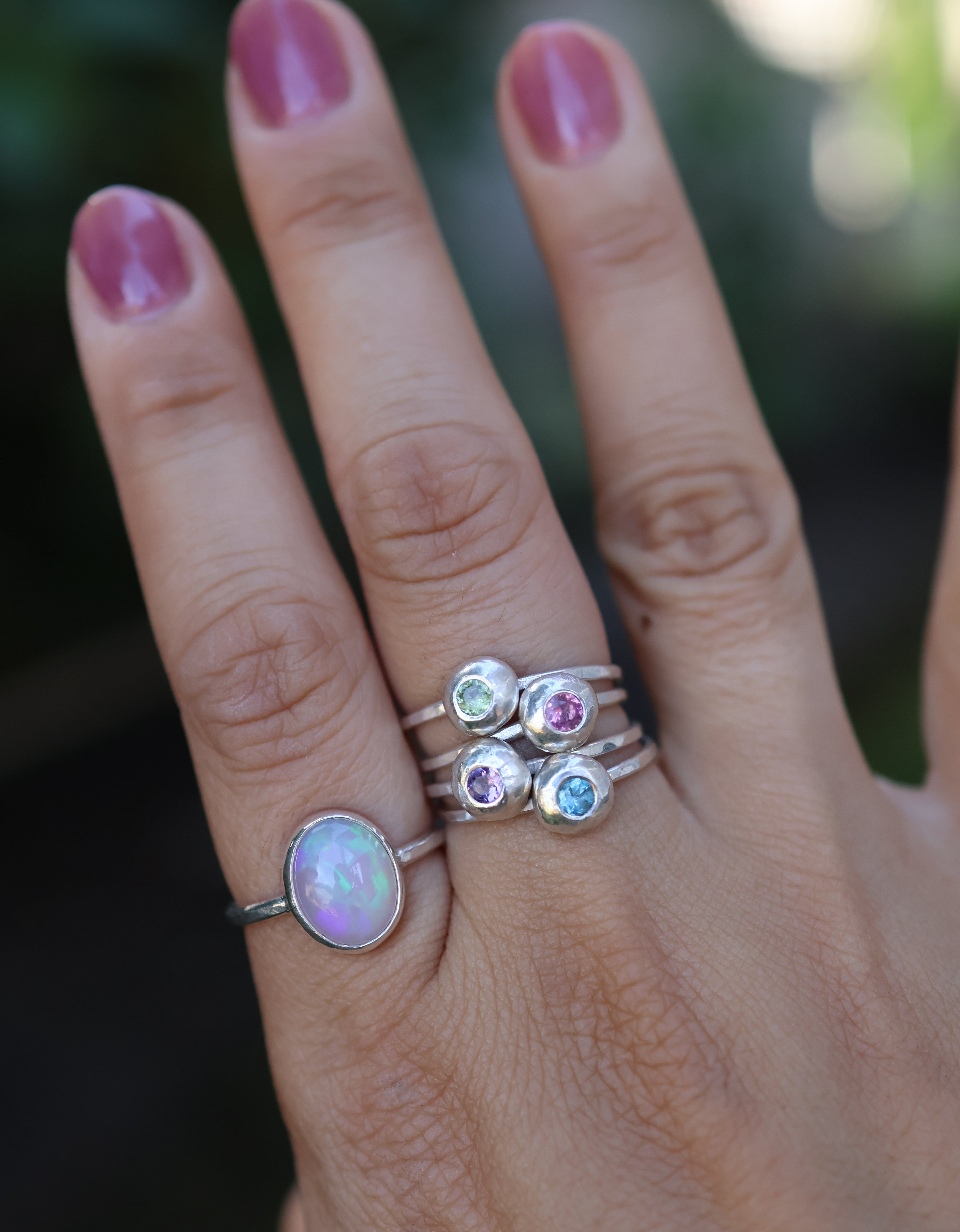 Hand wearing two silver rings with gemstones against a blurred natural background