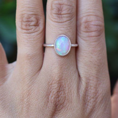 Hand wearing a ring with a colorful Ethiopian opal against a blurred natural background
