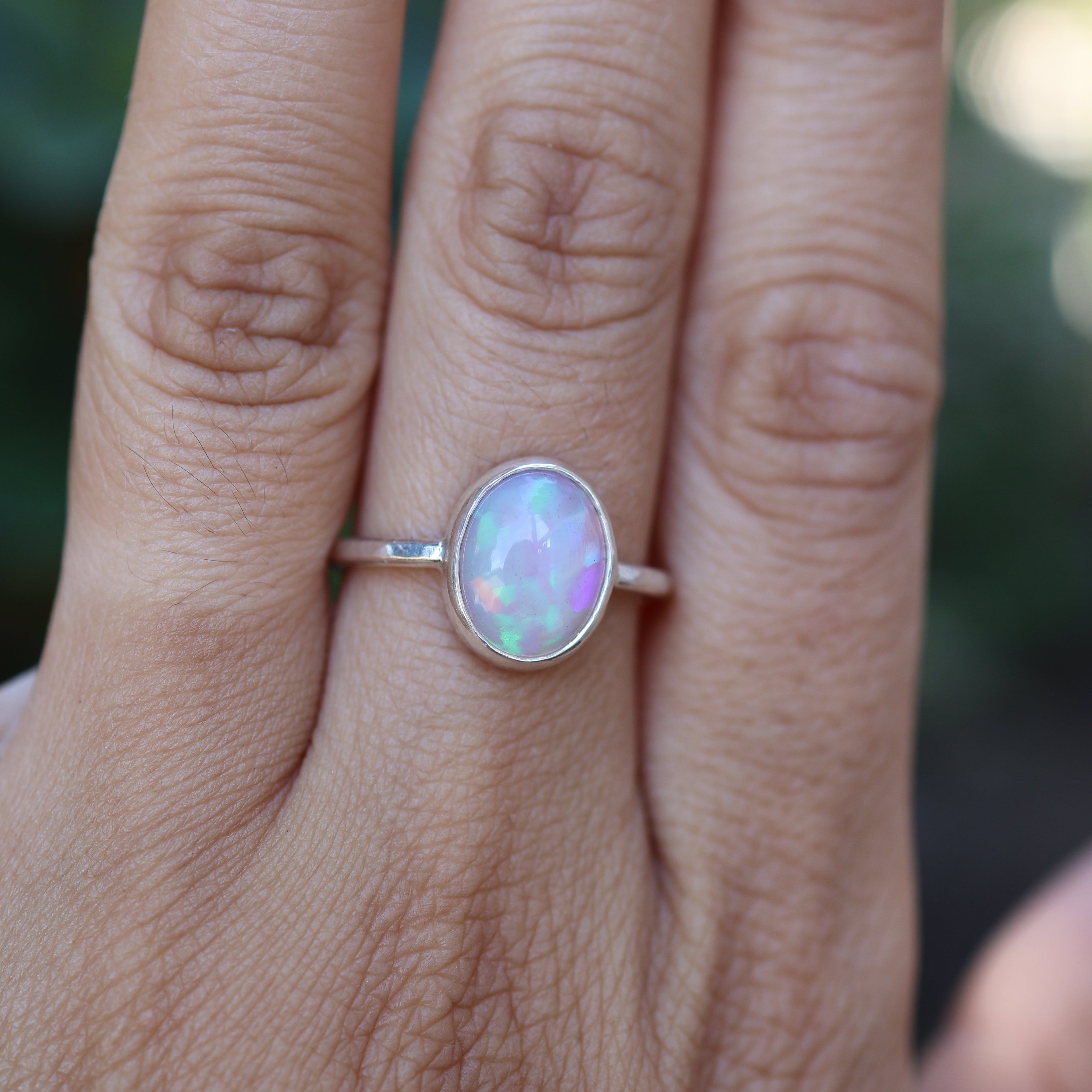 Hand wearing a silver ring with an opal stone against a blurred natural background