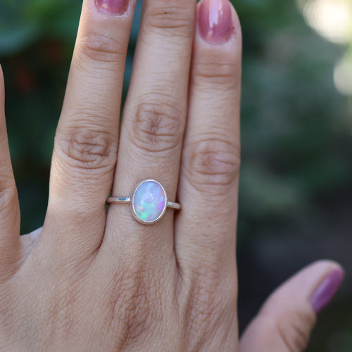 Hand wearing a silver ring with an opal stone against a blurred green background