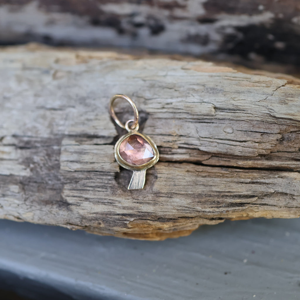 Gold pendant with a pink stone on a wooden surface