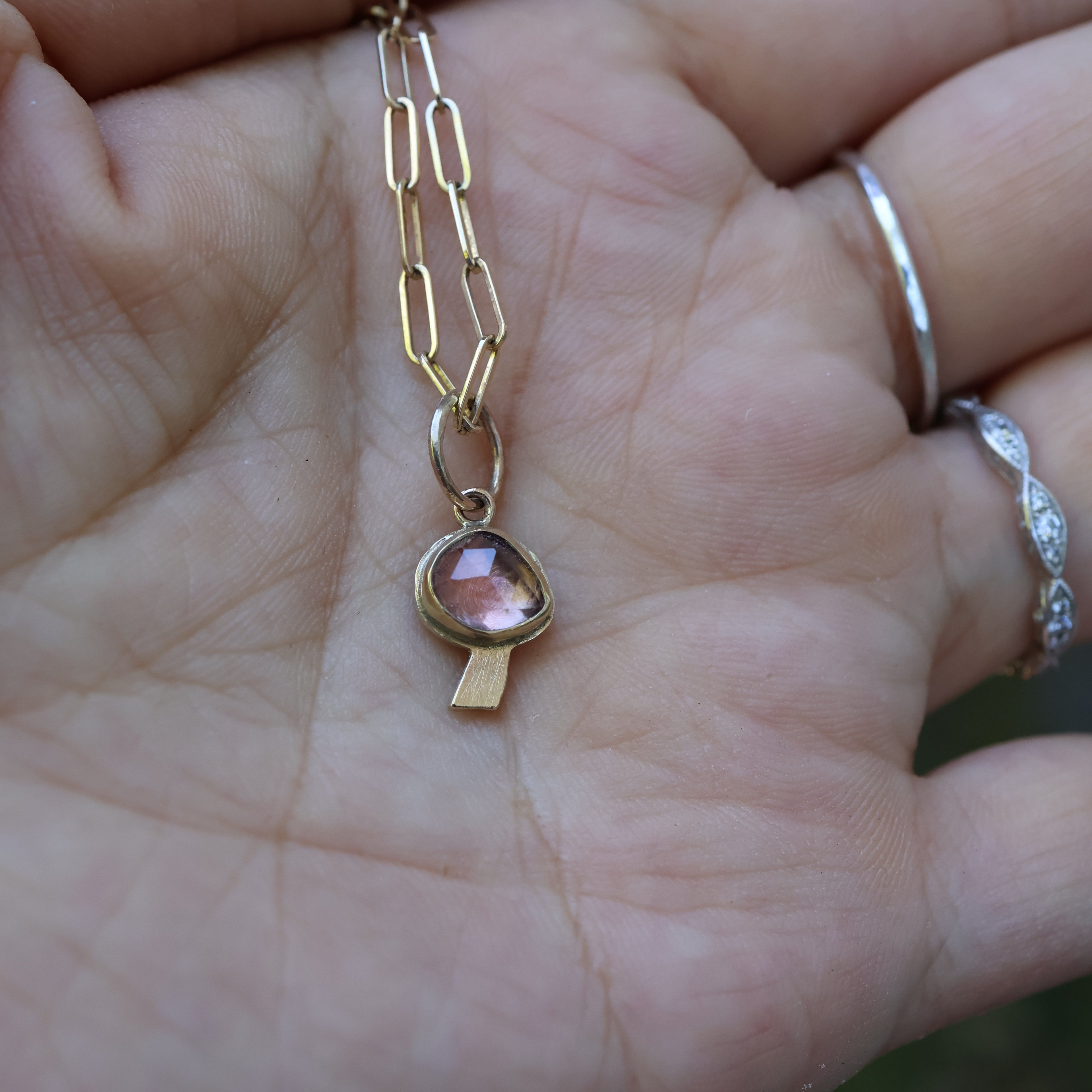 Gold necklace with a pink gemstone on a hand