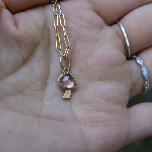 Gold necklace with a pink gemstone on a hand