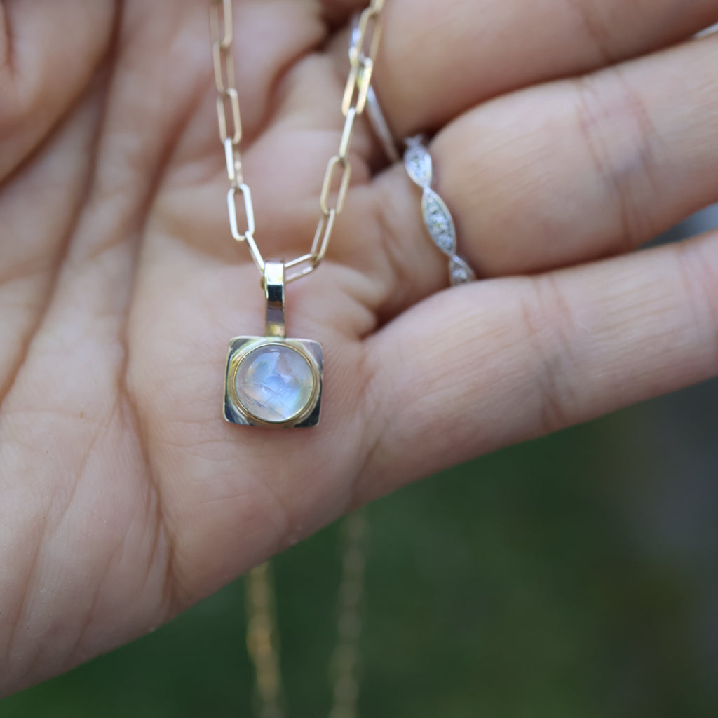 Gold necklace with a pendant held in a hand against a blurred natural background