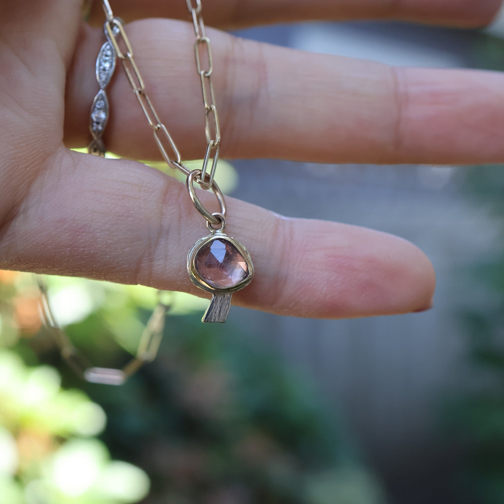 Hand holding a delicate necklace with a pink gemstone pendant against a blurred natural background