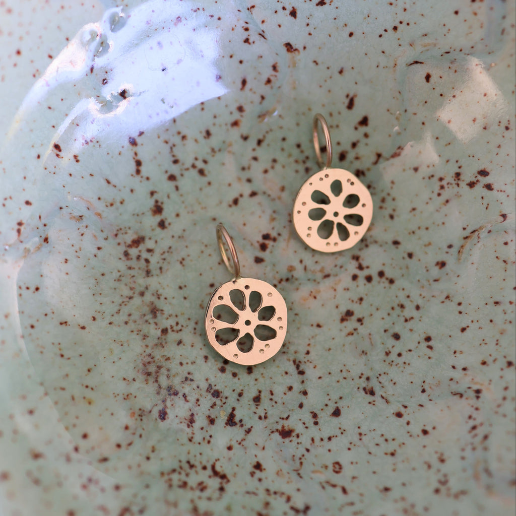 Two gold lotus root shaped pendants on a green ribbon on a textured green background