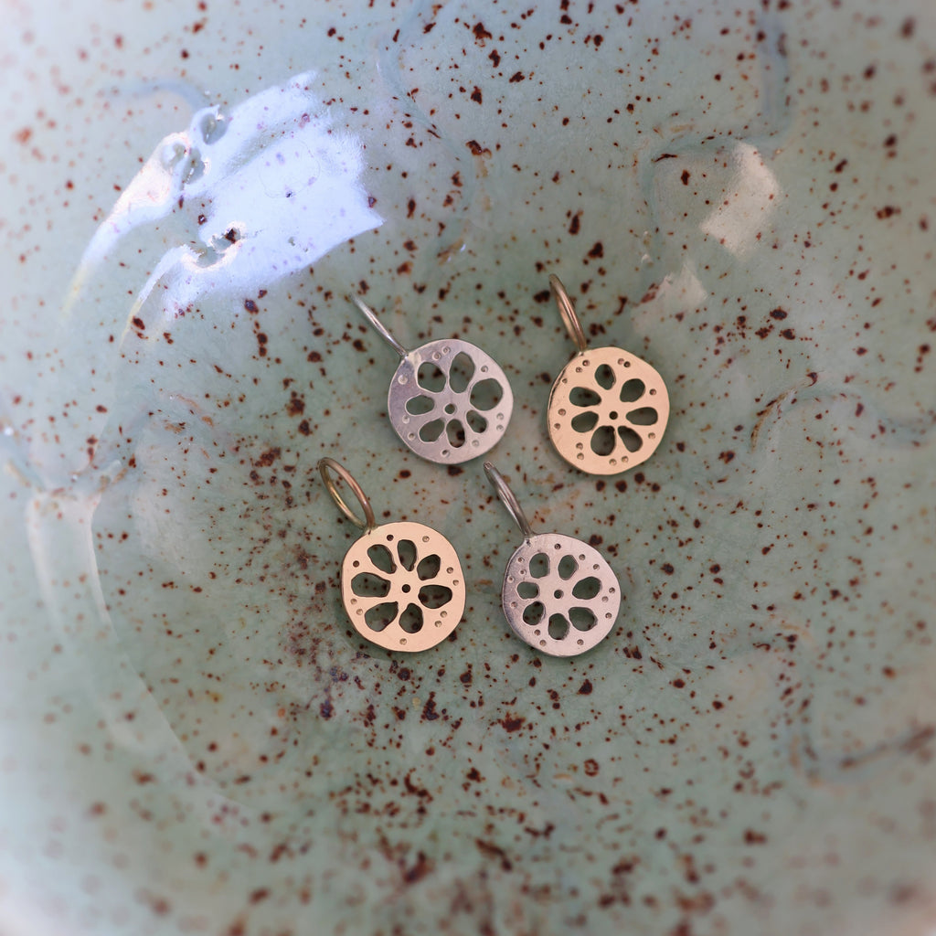 Four lotus root pendants, two gold and two silver, in a textured ceramic dish.