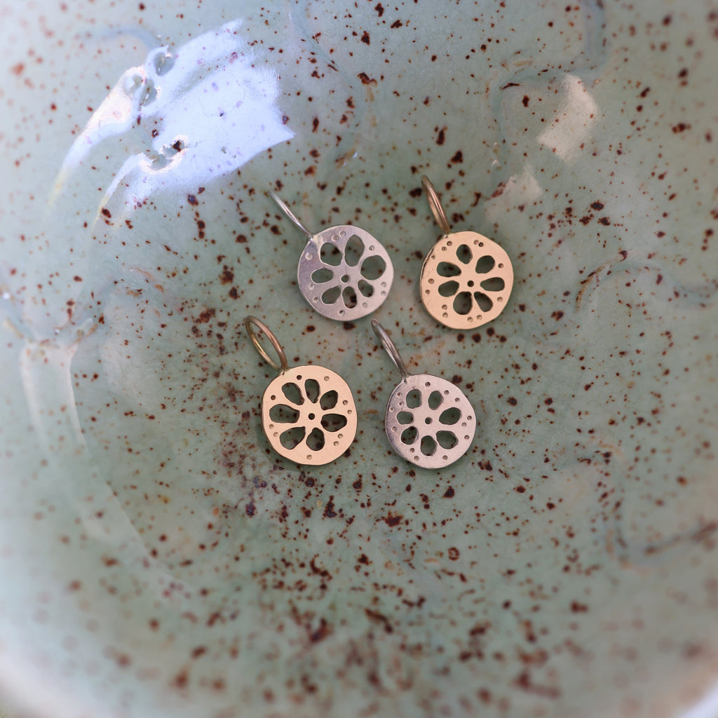 Four lotus root pendants, two gold and two silver, in a textured ceramic dish.