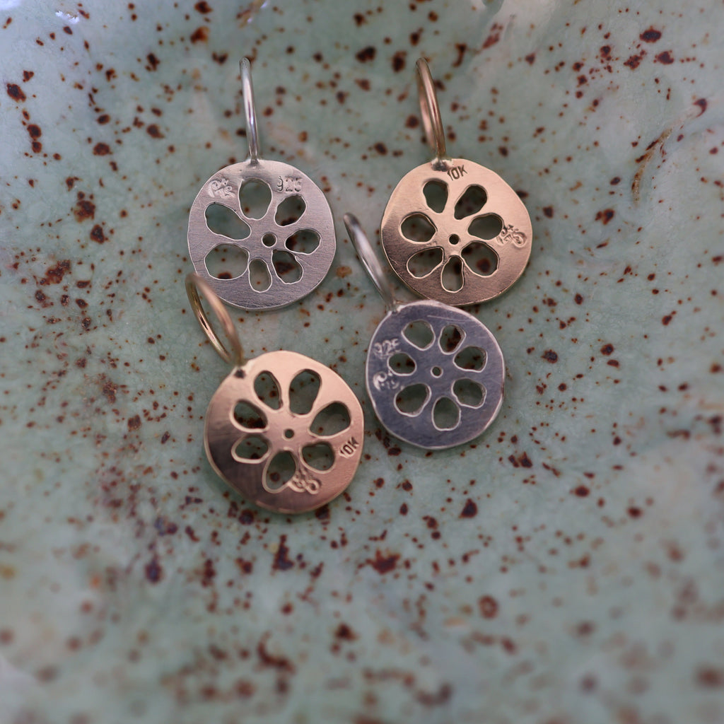 The back of four lotus root pendants, showing maker's mark and metal purity stamps, in a textured ceramic dish.