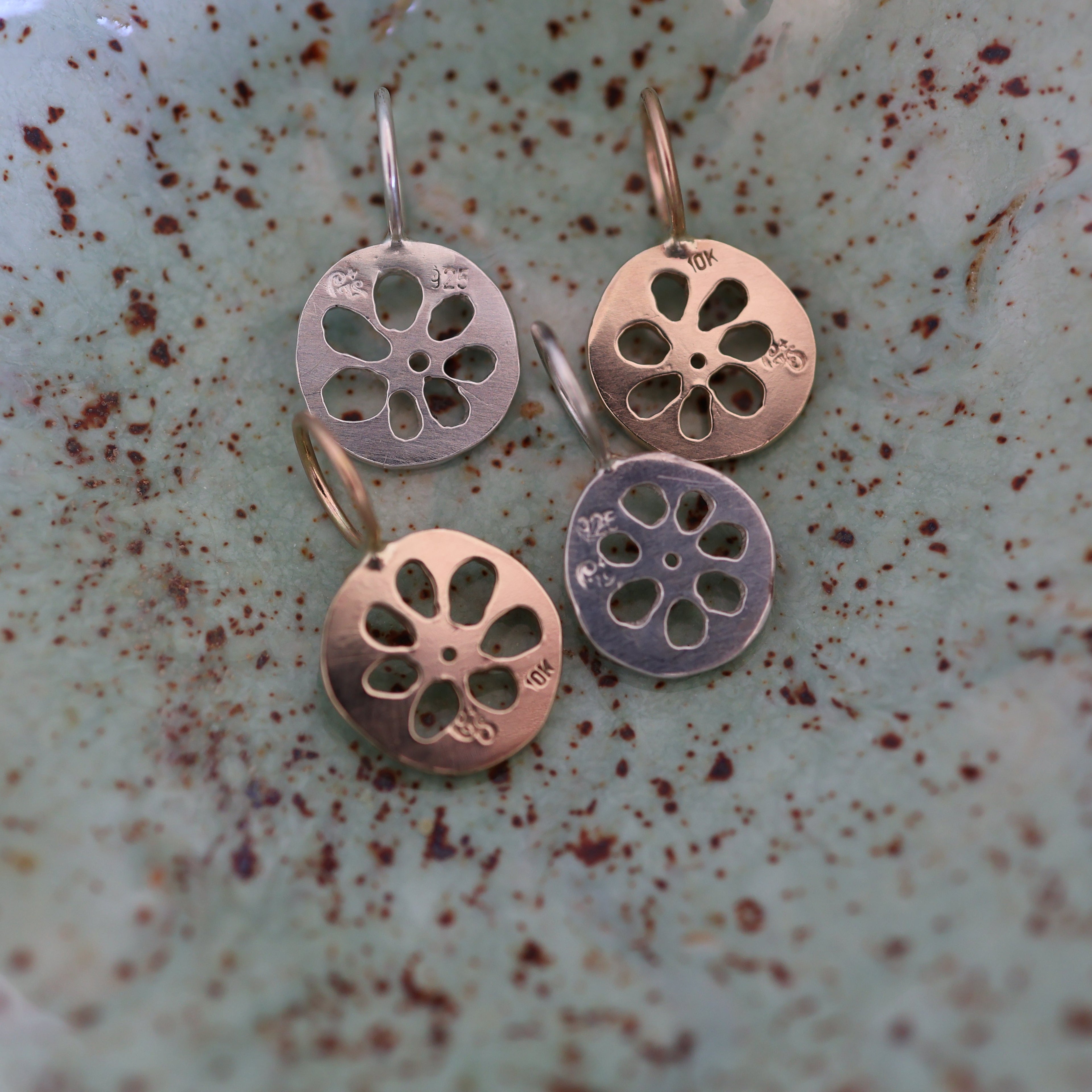 The back of four lotus root pendants, showing maker's mark and metal purity stamps, in a textured ceramic dish.