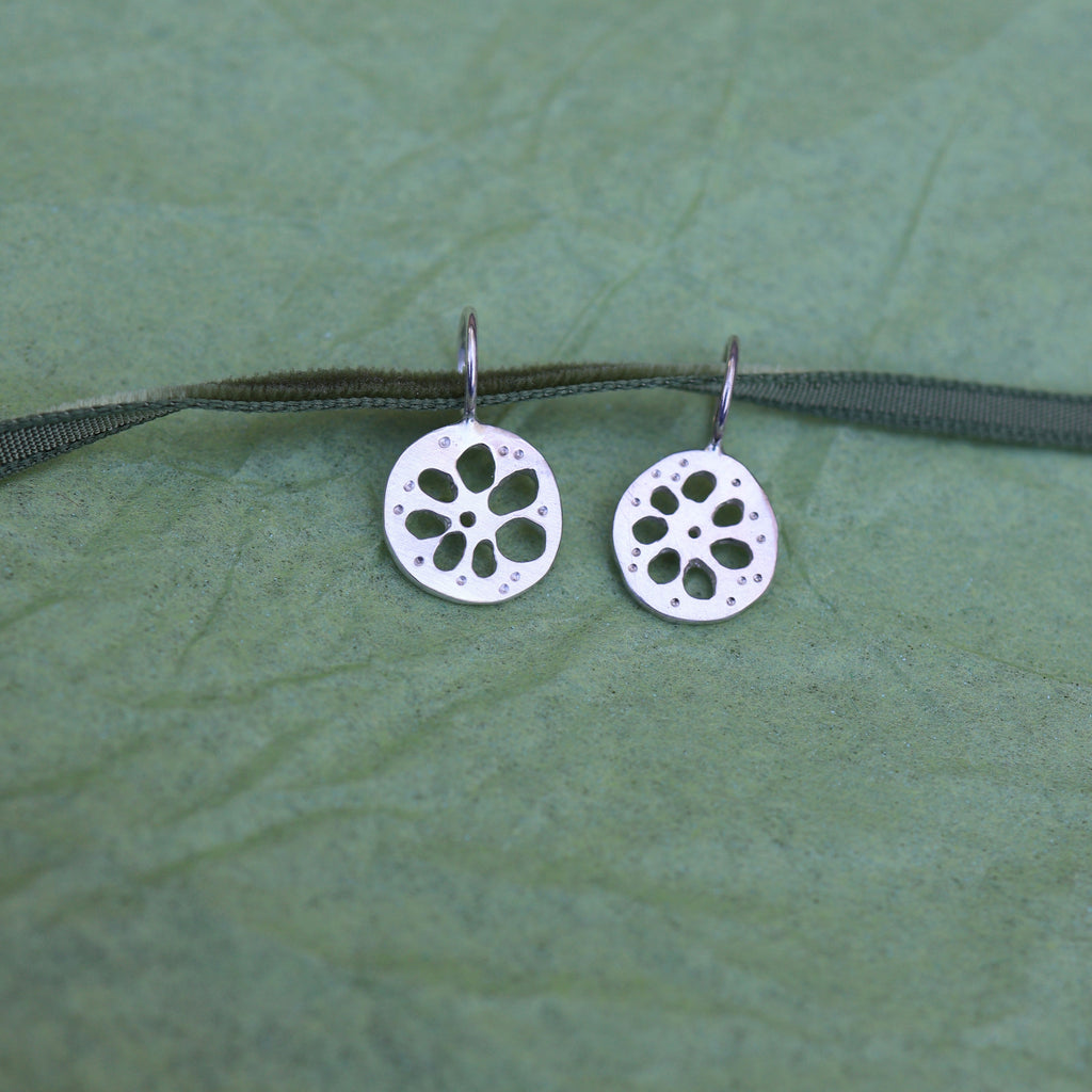 Two silver lotus root shaped pendants on a green ribbon on a textured green background