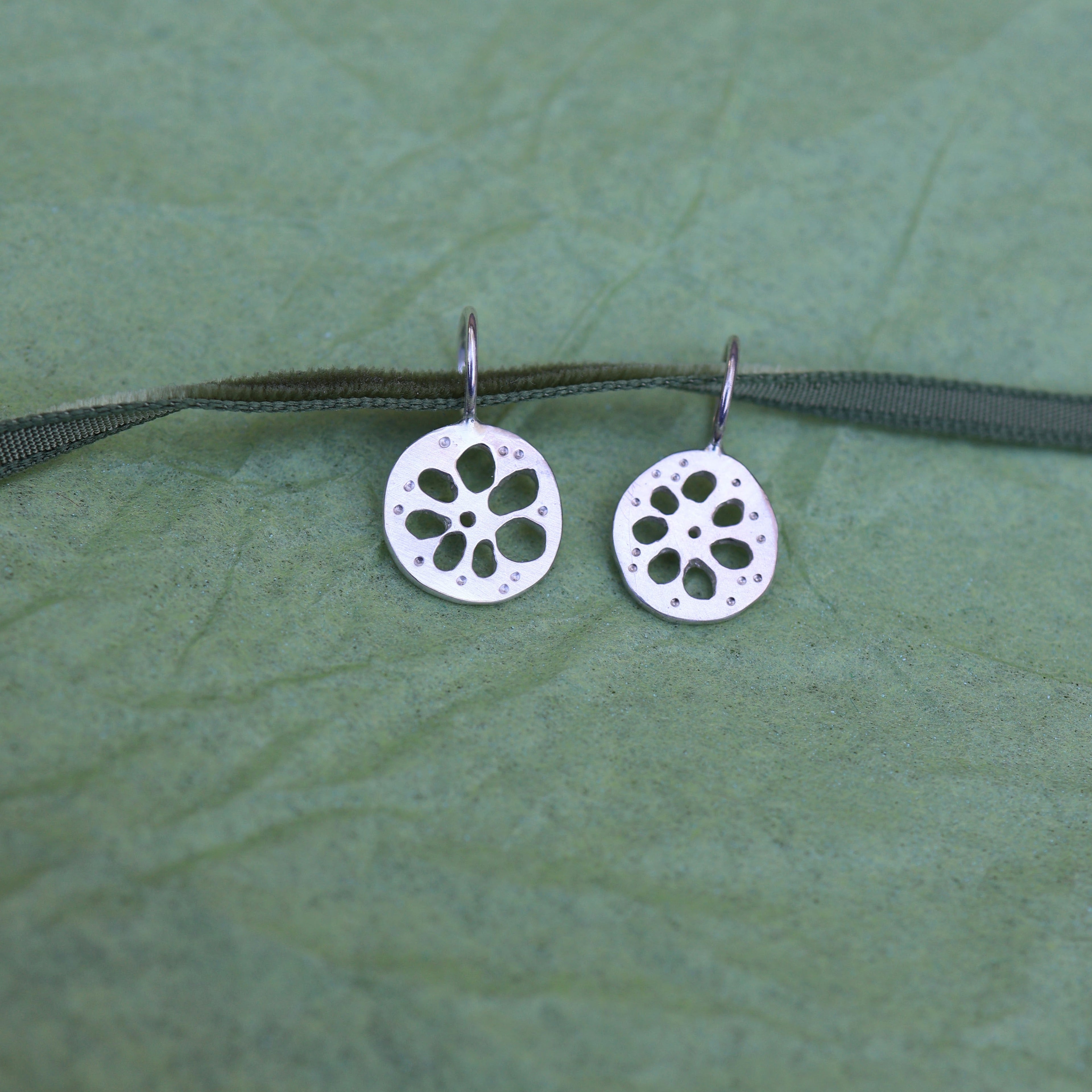 Two silver lotus root shaped pendants on a green ribbon on a textured green background