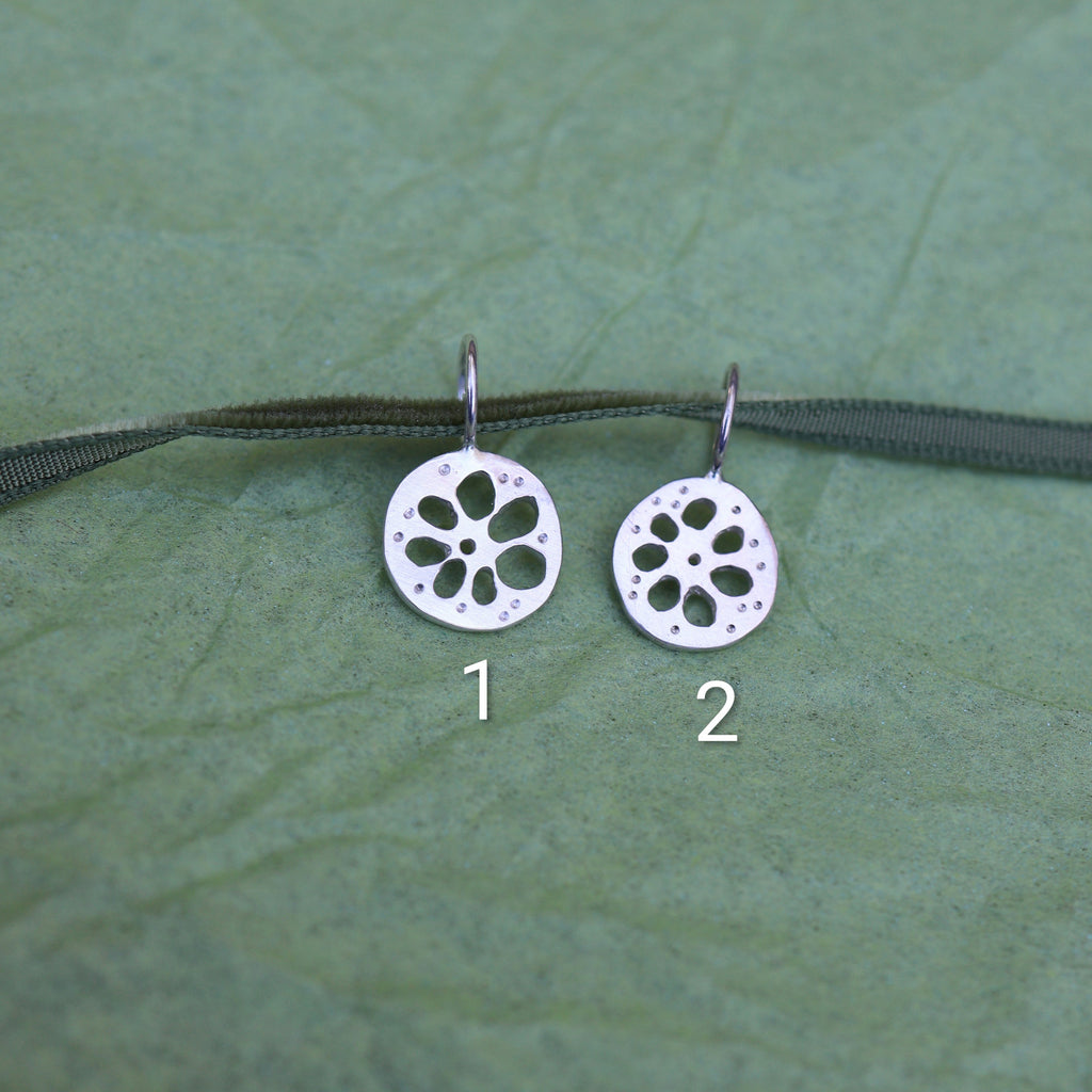 Two silver lotus root shaped pendants on a green ribbon on a textured green background
