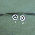 Two silver lotus root shaped pendants on a green ribbon on a textured green background