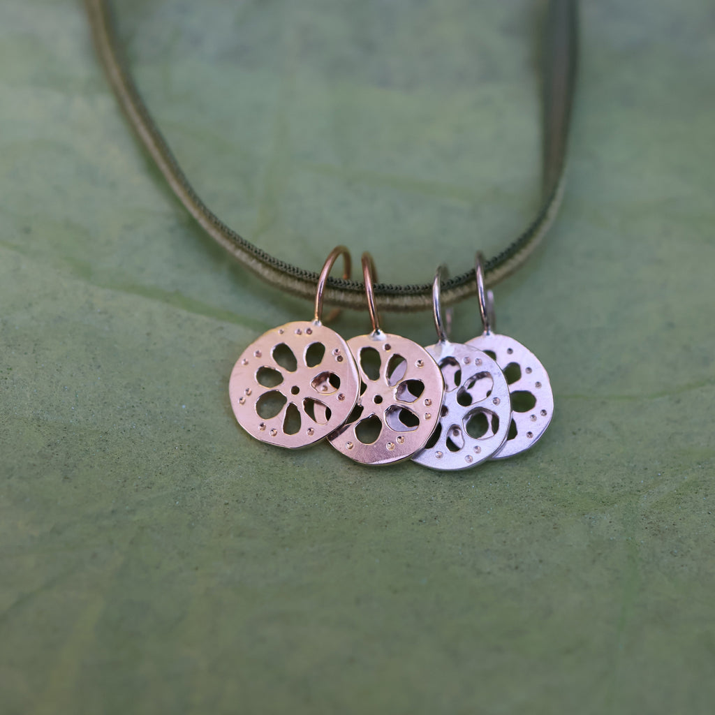 Four lotus root pendants, two gold and two silver, hanging from a thin green cord, displayed on a textured green surface.