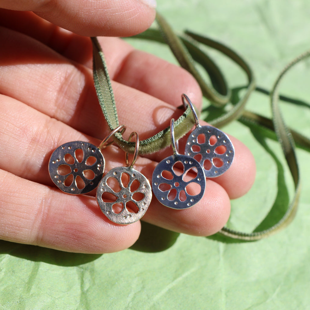 Four lotus root pendants, two gold and two silver, hanging from a thin green cord, displayed on a textured green surface.