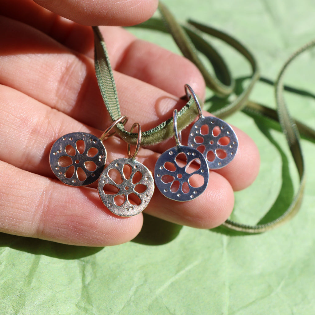 Four lotus root pendants, two gold and two silver, hanging from a thin green cord, displayed on a textured green surface.