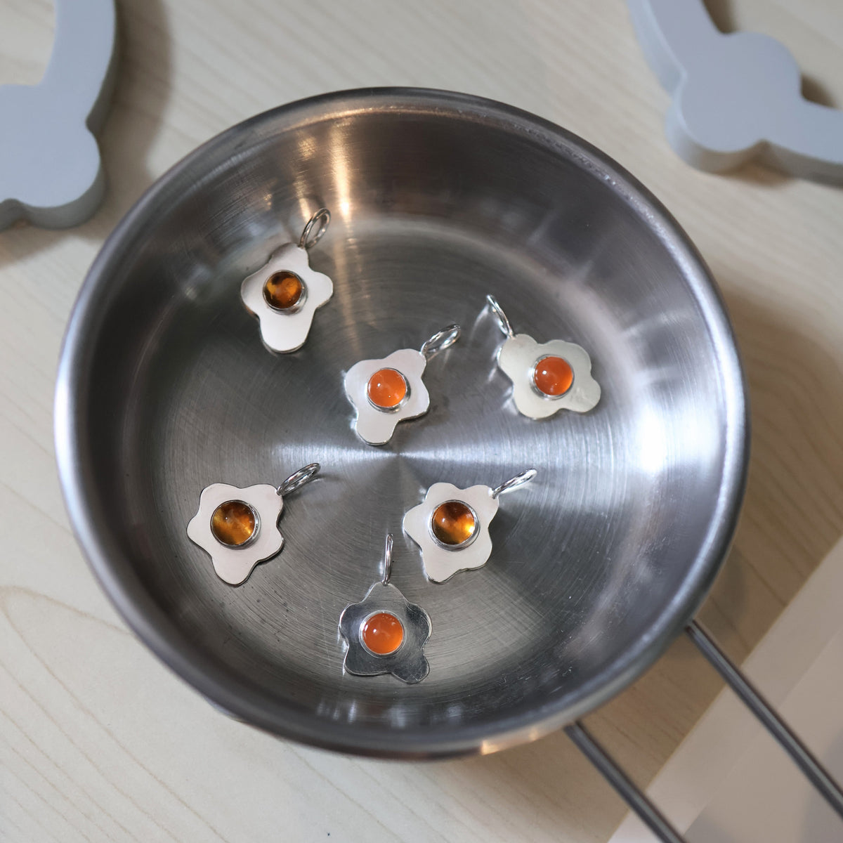 a small pan with six fried egg pendants made of silver and orange gemstones