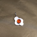 a pendant in the shape of a sunny side up fried egg with a orange center stone