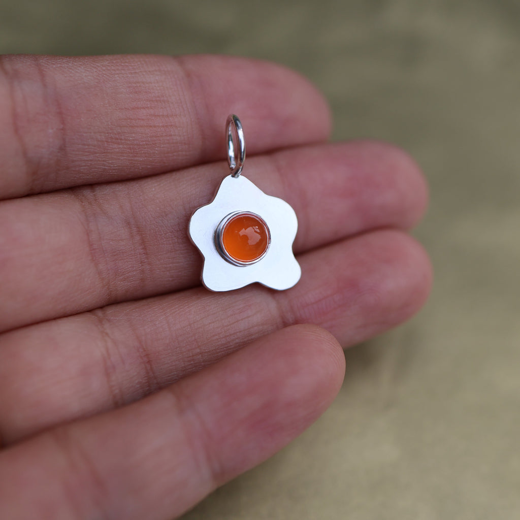 a pendant in the shape of a sunny side up fried egg with a orange center stone