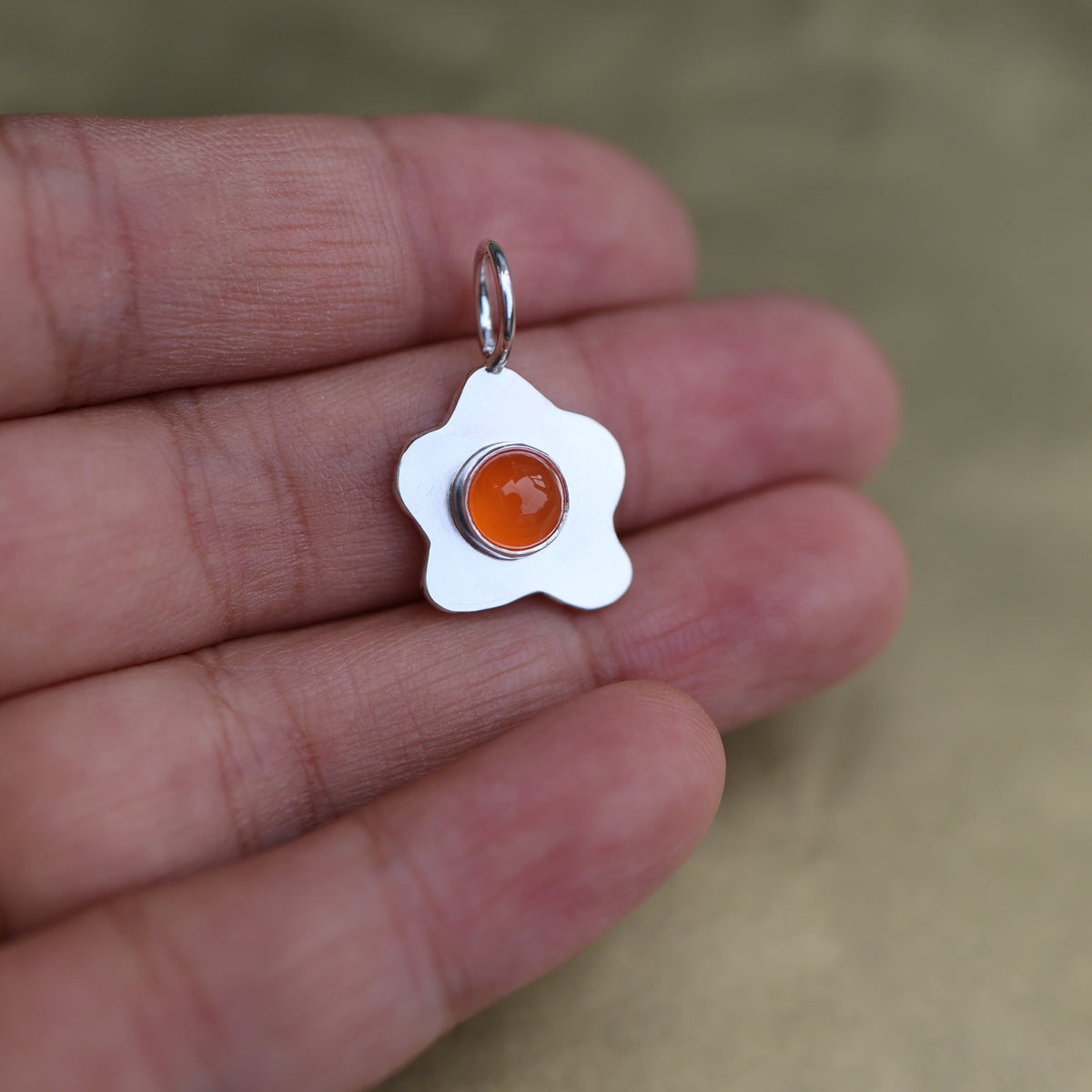 a pendant in the shape of a sunny side up fried egg with a orange center stone