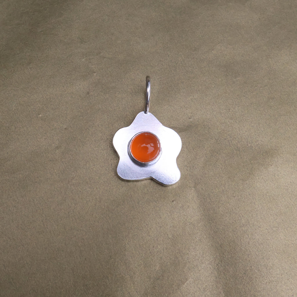 a pendant in the shape of a sunny side up fried egg with a orange center stone