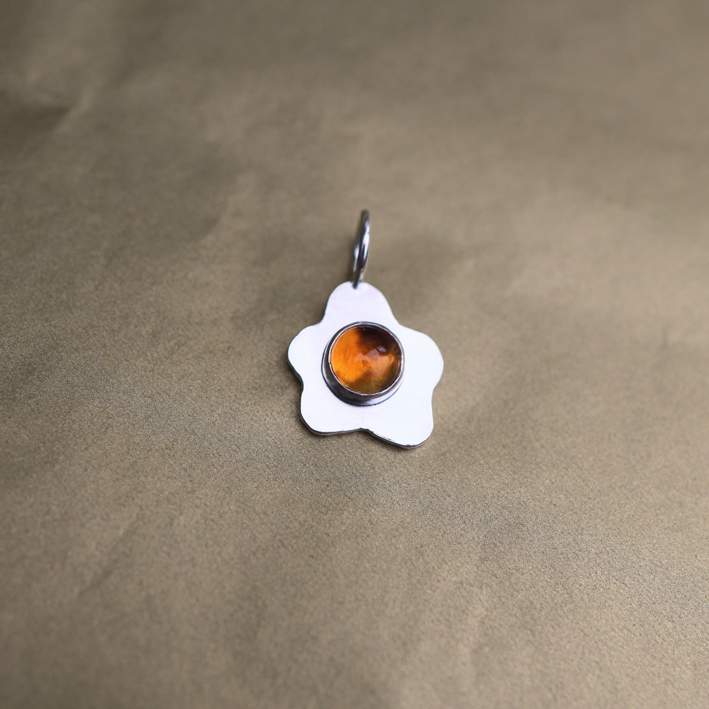a pendant in the shape of a sunny side up fried egg with a orange center gemstone