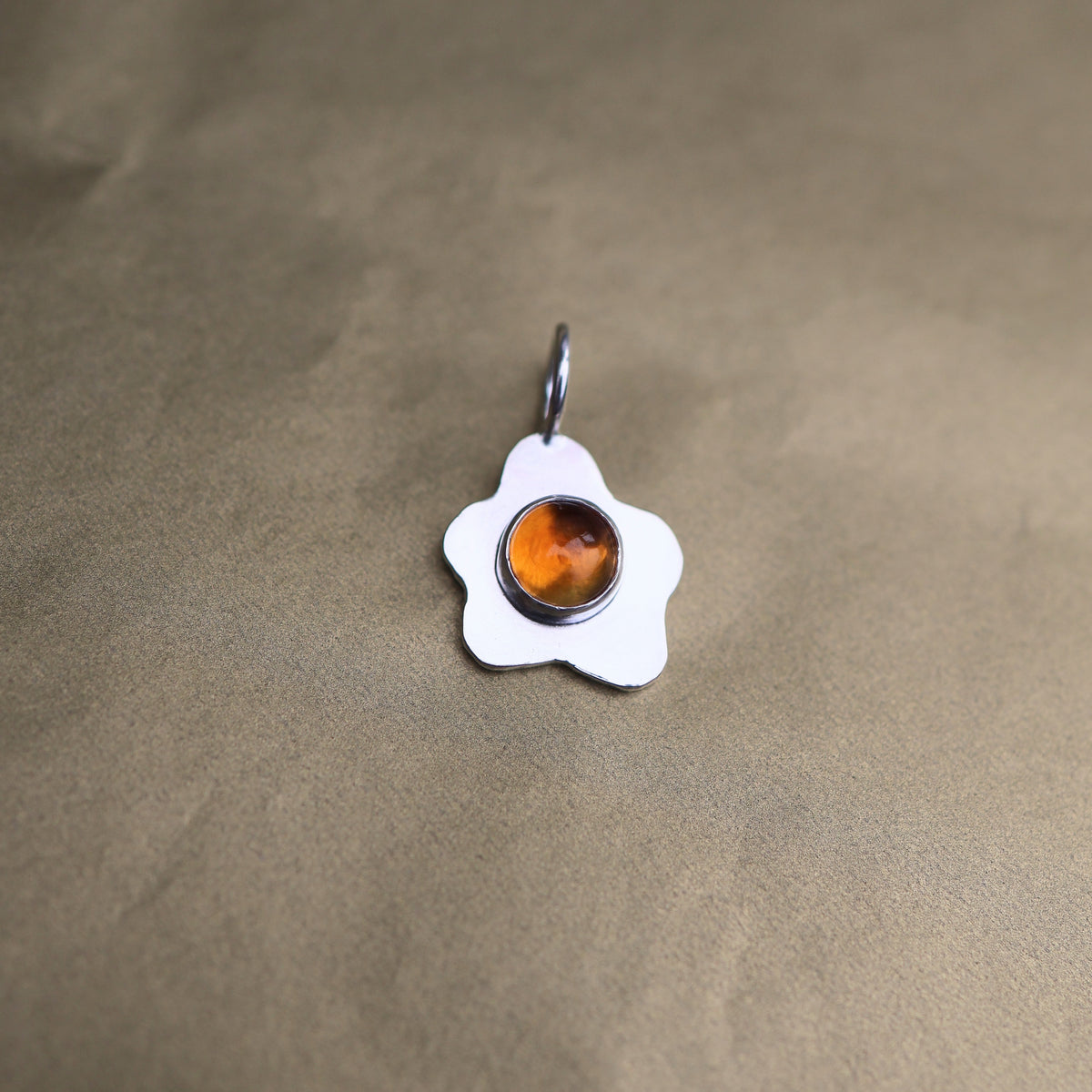 a pendant in the shape of a sunny side up fried egg with a orange center gemstone