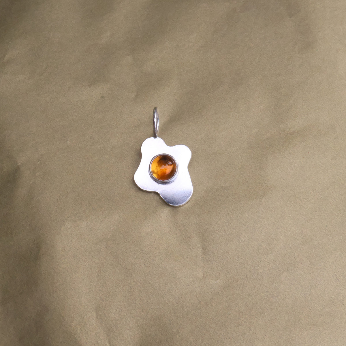 a pendant in the shape of a sunny side up fried egg with a orange center gemstone