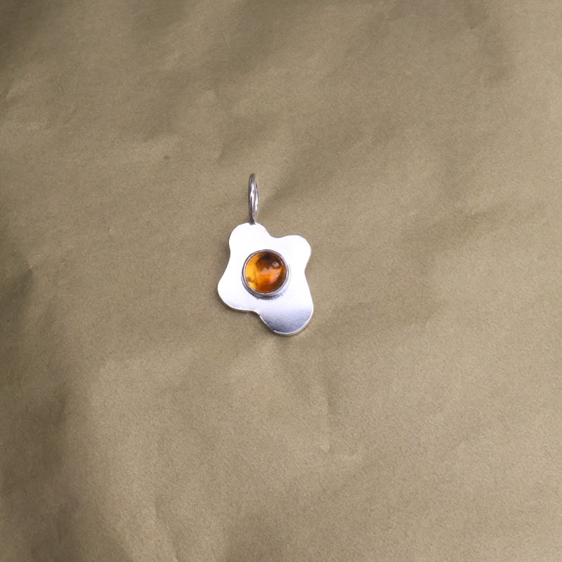 a pendant in the shape of a sunny side up fried egg with a orange center gemstone