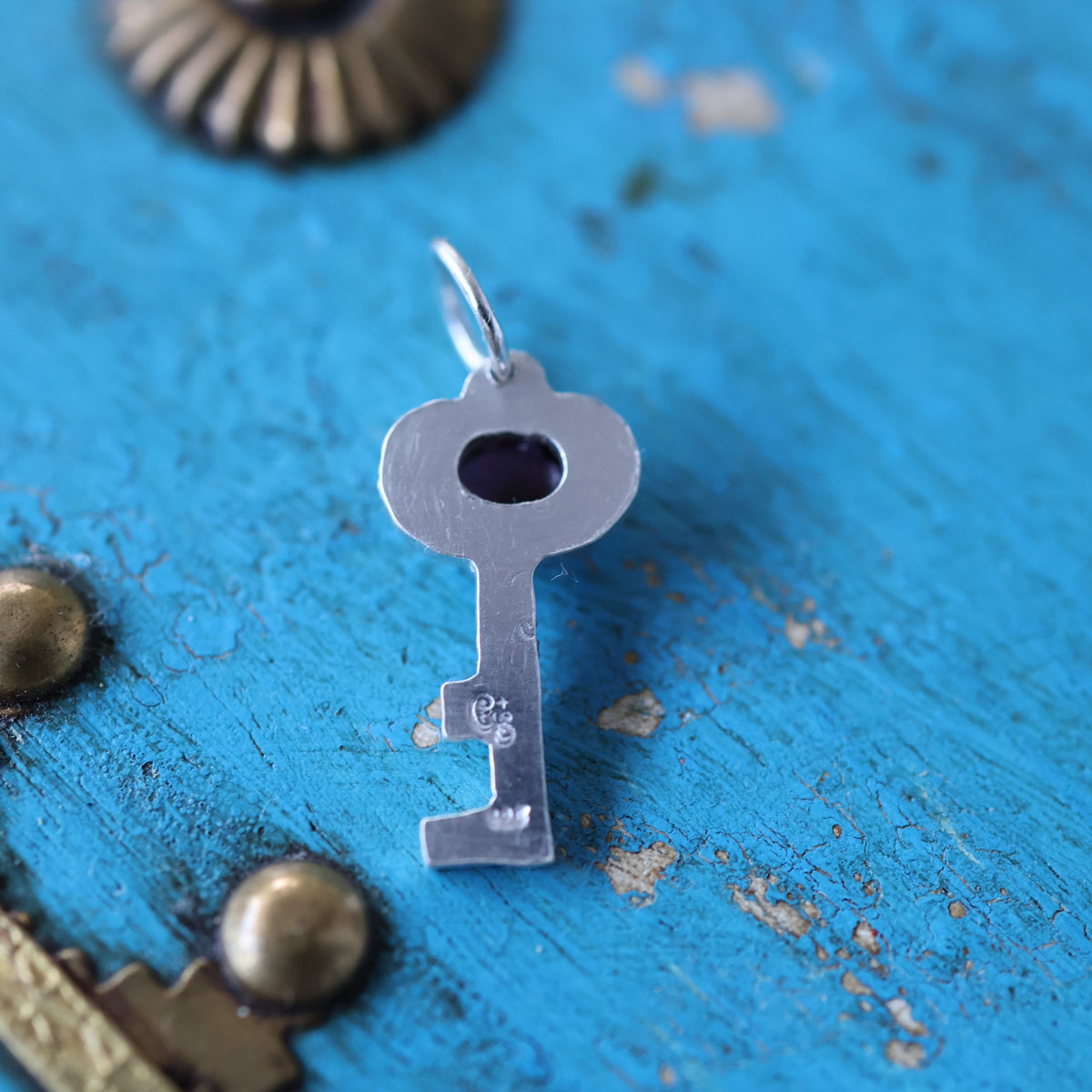the back of a key-shaped silver pendant, showing makers mark and quality stamps