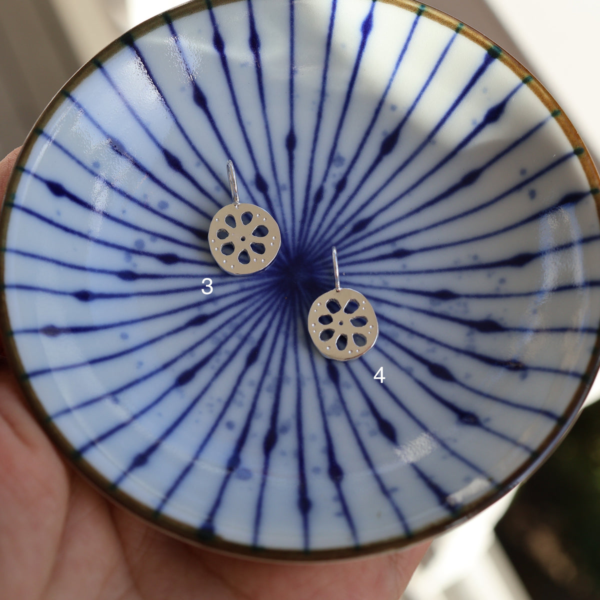 two silver lotus root charms in a blue dish held by a hand