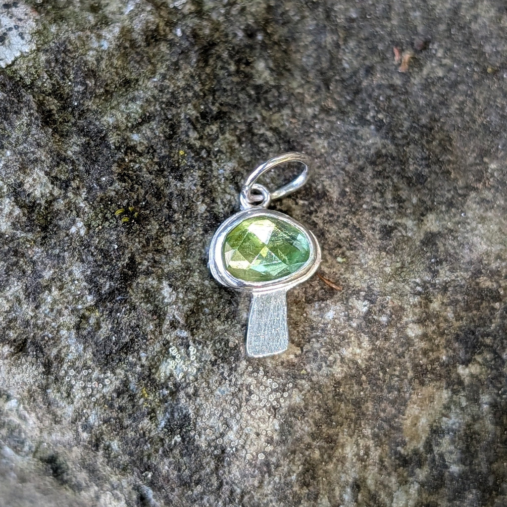 Silver mushroom shaped pendant with a green gemstone on a textured stone surface