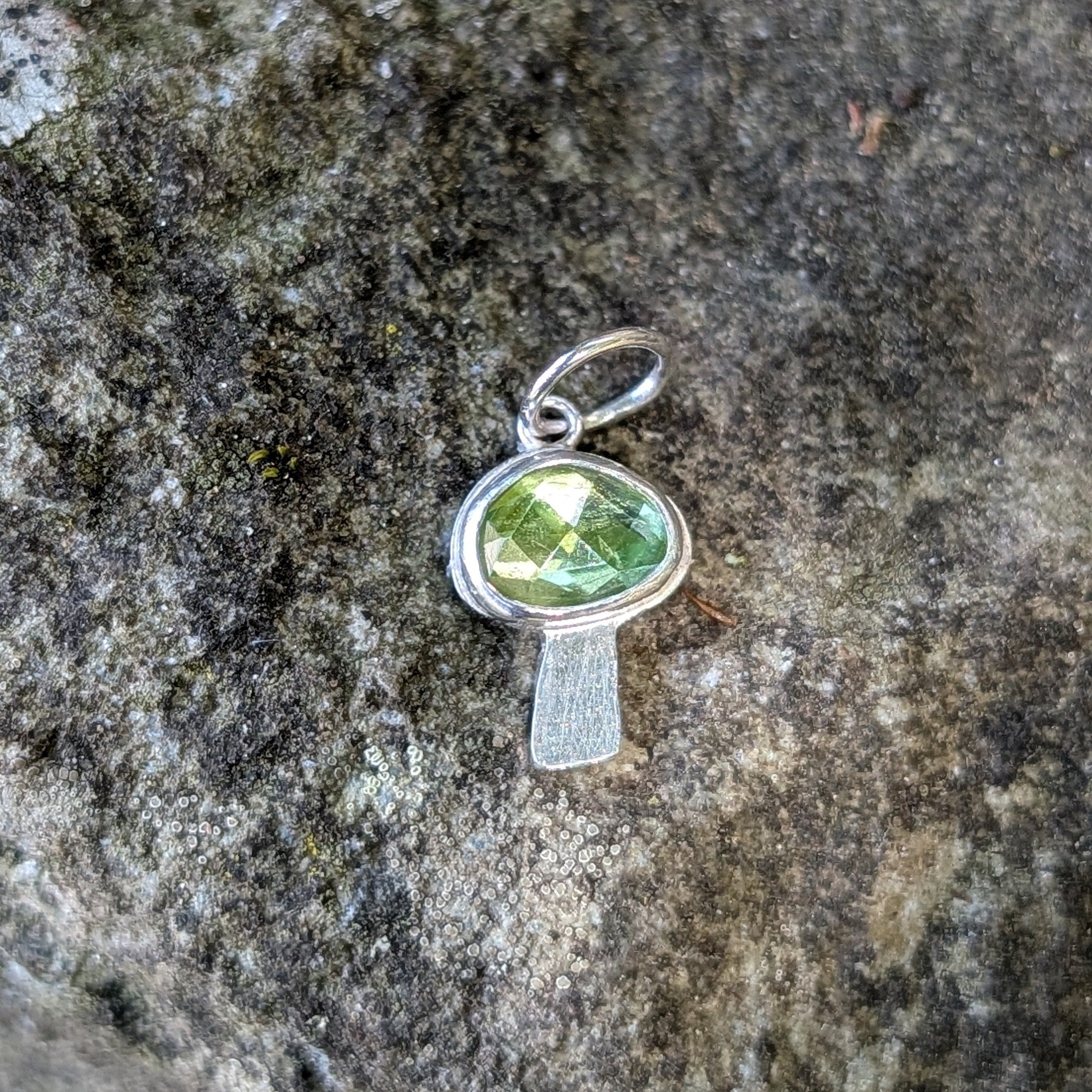 Silver mushroom shaped pendant with a green gemstone on a textured stone surface