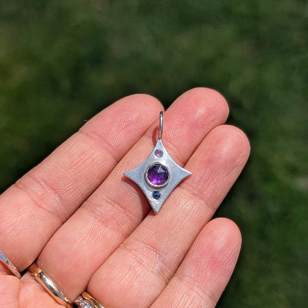 Silver star-shaped pendant with a purple gemstone held in a hand against a green background