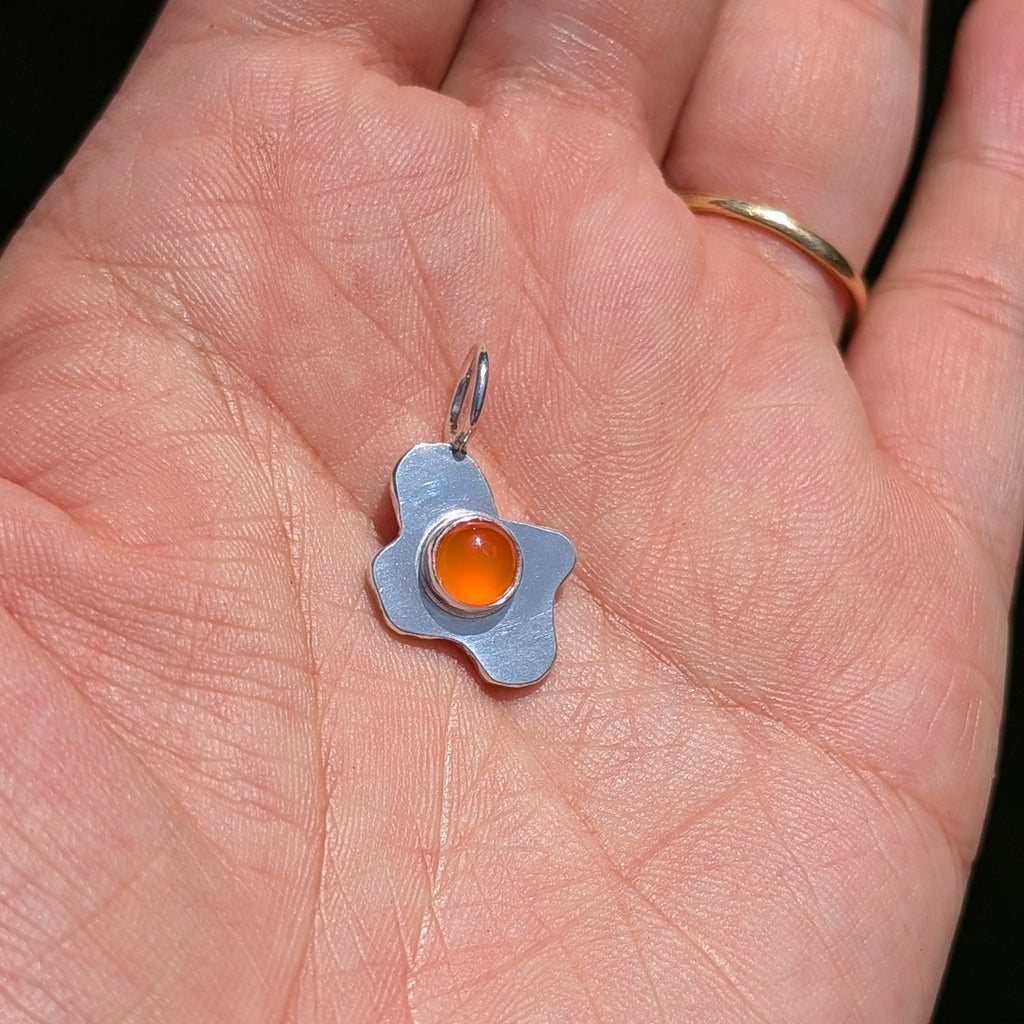 Small pendant resembling a cracked egg with an orange yolk on a hand.