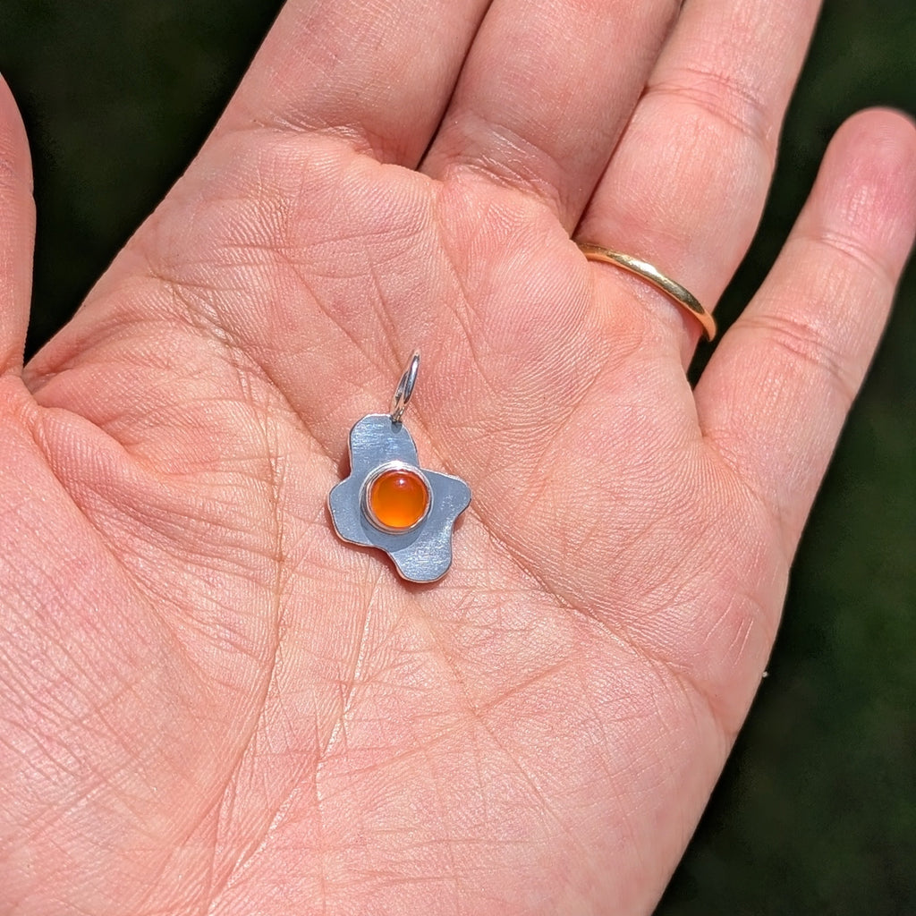 Hand holding a fried egg pendant with a carnelian stone 