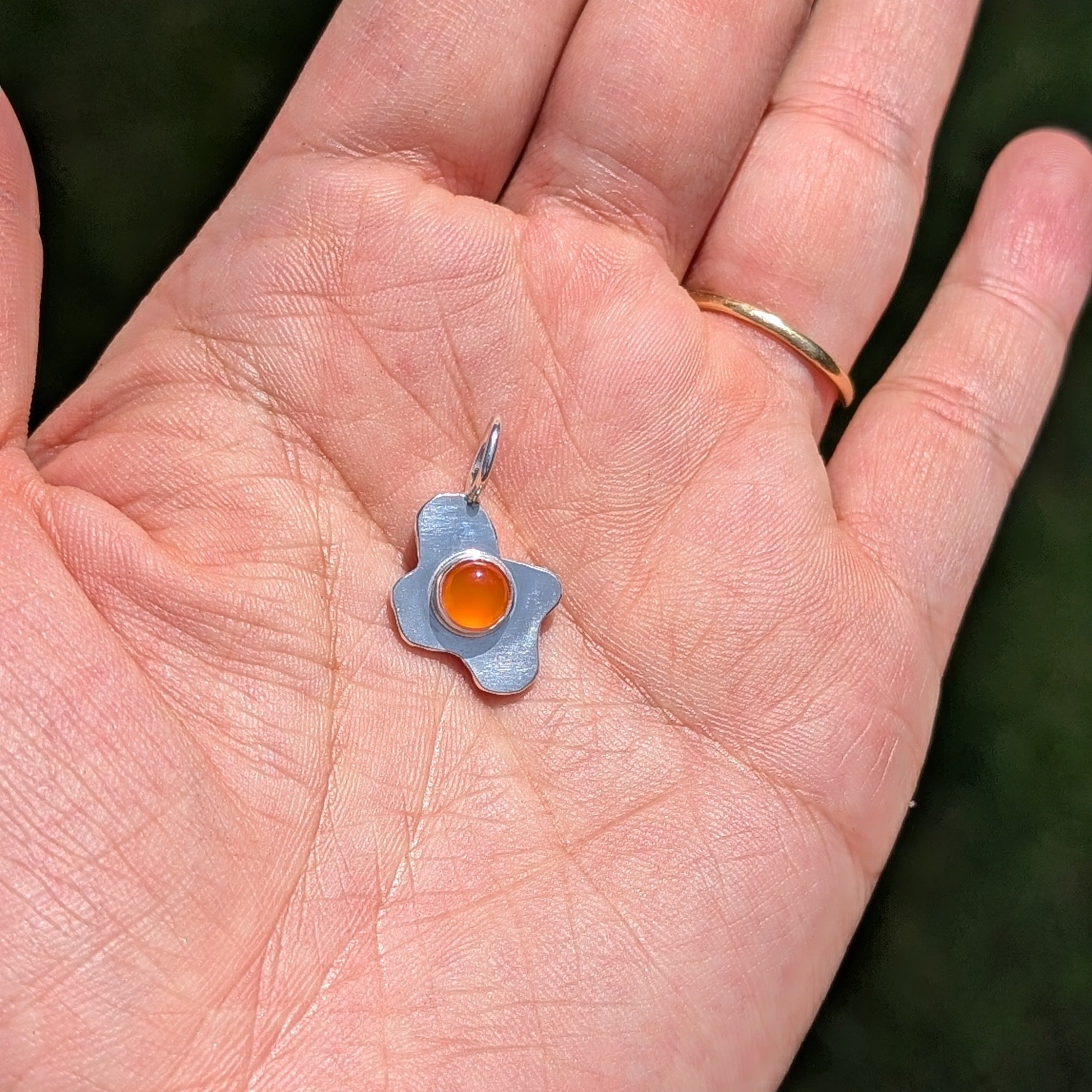 Hand holding a fried egg pendant with a carnelian stone 