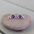 Pair of silver earrings with purple gemstones on a stone surface