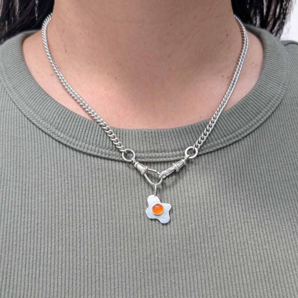 Necklace with a fried egg pendant worn by a person on a plain background
