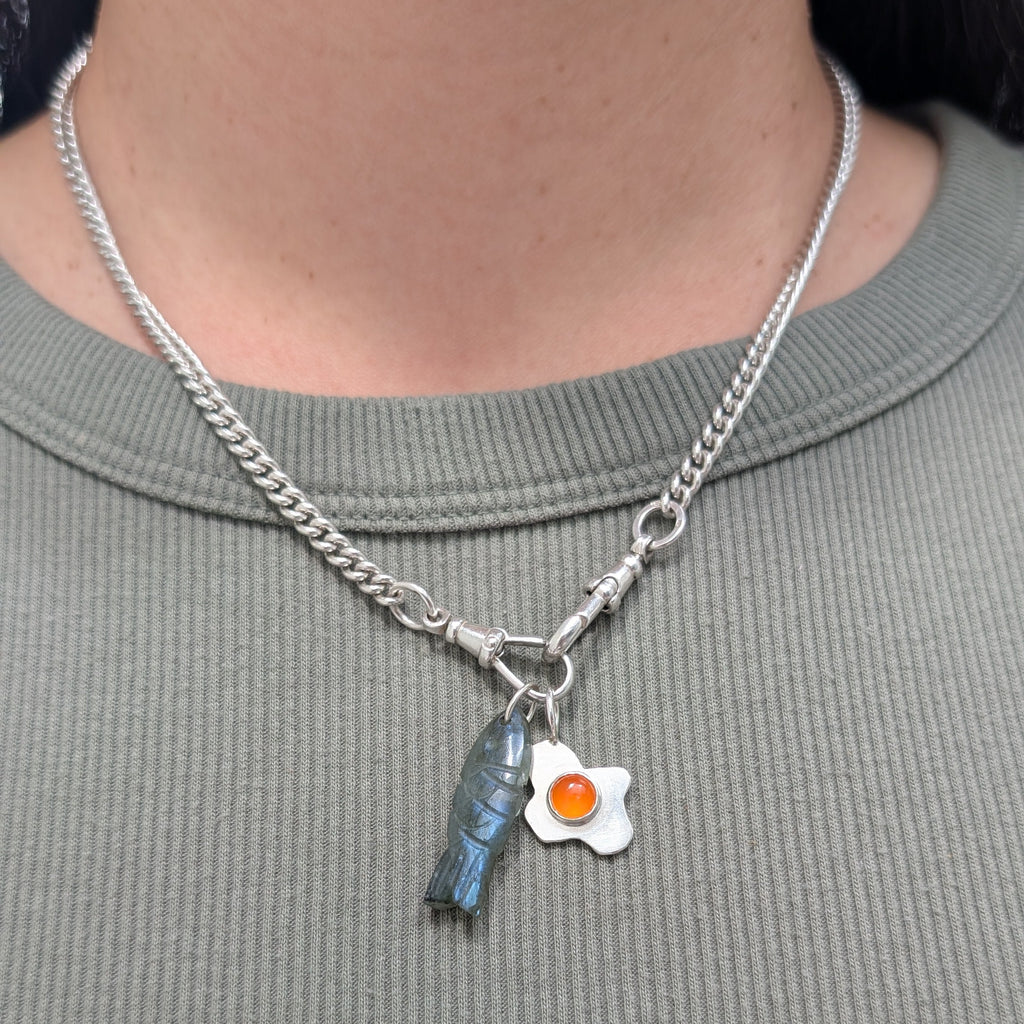 silver necklace with a fish pendant and fried egg pendant