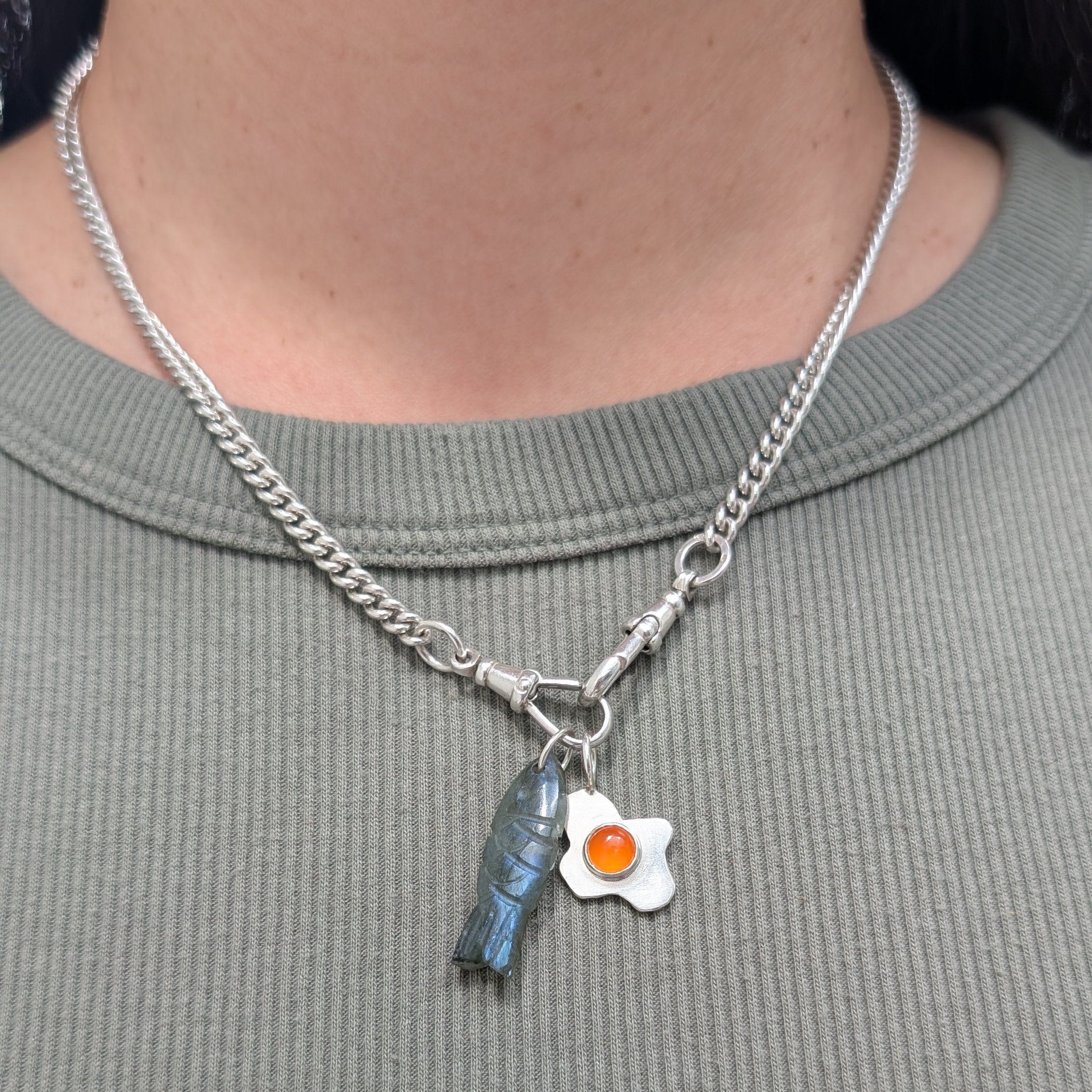 silver necklace with a fish pendant and fried egg pendant