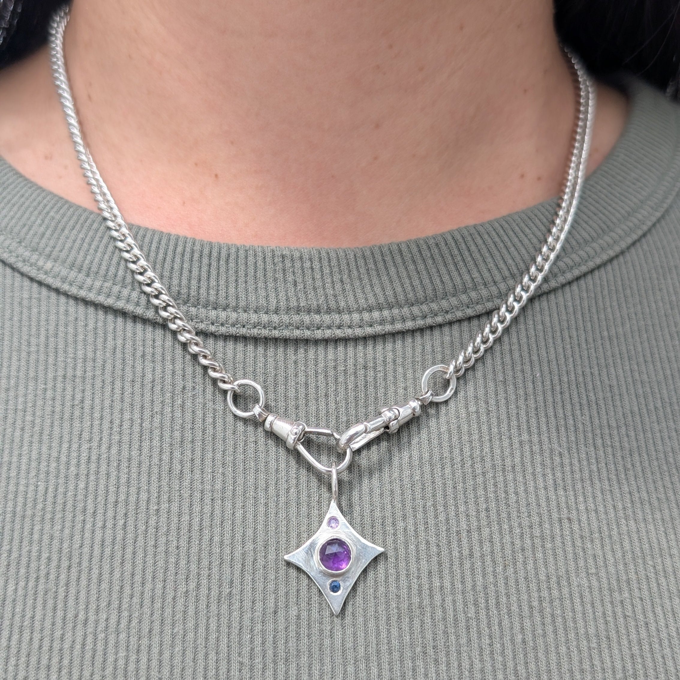Silver necklace with a star-shaped pendant featuring a purple gemstone worn by a person.