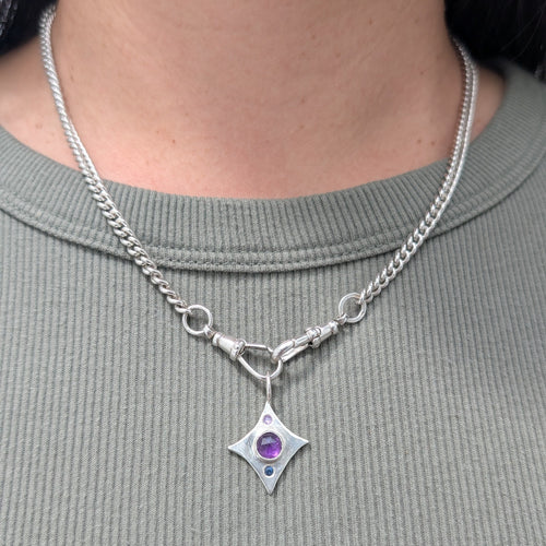 Silver necklace with a star-shaped pendant featuring a purple gemstone worn by a person.