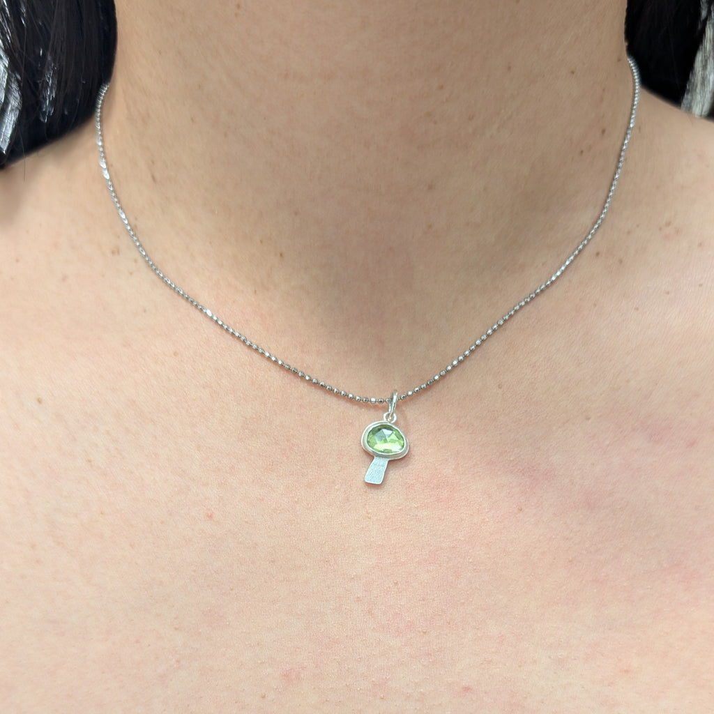Necklace with a peridot mushroom pendant worn by a person